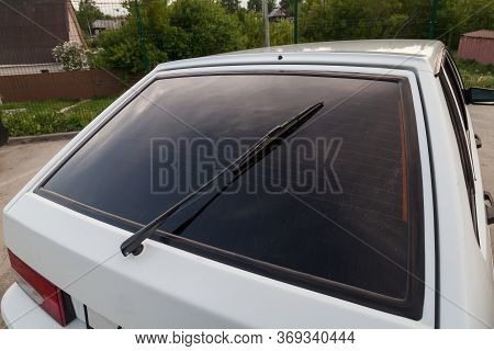 Closeup Of A Clean Rear Tinted Black Glass Of A Russian White Car With A Wiper And A Red Brake Light