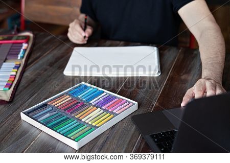Man Artist Painting With Pencil And Pastel Crayon On Paper In Front Of Laptop. Learning Painting Onl
