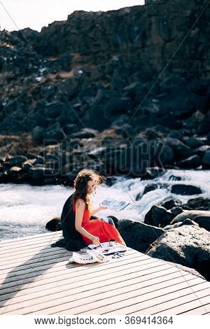 The Girl Artist Paints A Picture In The Album With Watercolors. Near Ehsaraurfoss Waterfall, Ehsarau