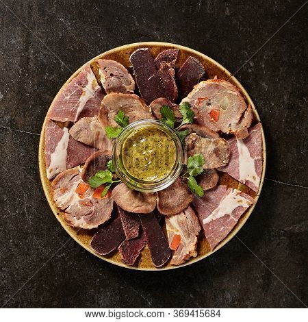 Meat plate with mustard on black marble table. Charcuterie. Cold boiled pork, sujuk, beef tongue and pastrami on plate. Meat products assortment. French cuisine. Culinary art. Traditional dish