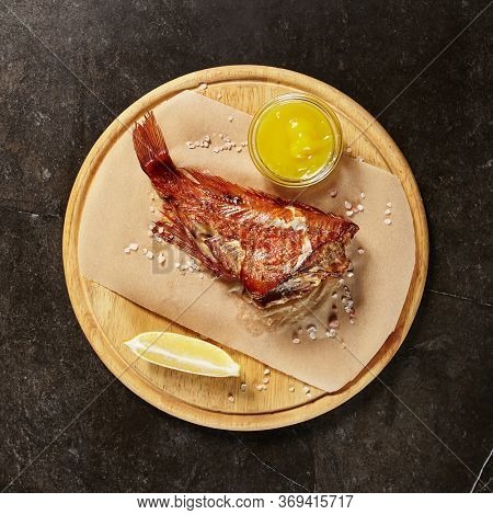 Perch served on piece of parchment and wooden board. Red fish portion on black marble table. Fancy seafood dish. Restaurant main course meal. Exquisite repast. Gourmet food serving