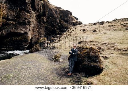 Portrait Of A Groom Leaning On A Stone In A Moss, Next To A Rocky Cleft With A Mountain River. Desti