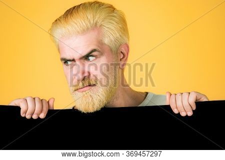 Serious Man Holding Big Black Poster Isolated On Yellow Background