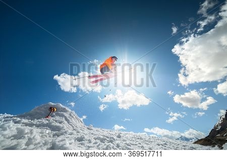A Young Stylish Man In Sunglasses And A Cap Performs A Trick In Jumping With A Kicker Of Snow Agains