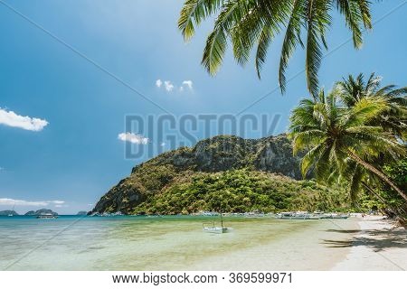 Palm Trees And Beautiful Scenery Of Corong Corong Beach With Traditional Boats, Mountain And Blue Sk