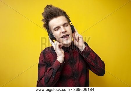 Young Energetic Guy Listens To Music On Headphones And Sings A Song On Yellow Isolated Background