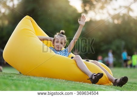 Outdoor Activity Concept, Boy Sitting On An Air Sofa, Welcomes, Raising His Hand Up