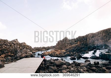 A Guy And A Girl Are Sitting Embracing On A Bridge Near Ehsaraurfoss Waterfall, Ehsarau River, Natio