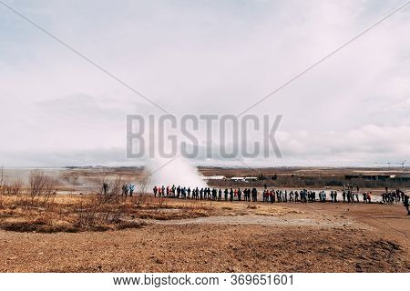 Tourists Look At The Eruption Of A Geyser. Geyser Valley In Southwest Of Iceland. The Famous Tourist