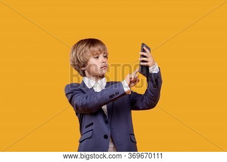 A Little Boy Uses A Mobile Phone. A Boy In A White Shirt.