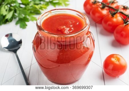 Tomatoes In Their Own Juice Or Tomato Paste In A Glass Jar And Fresh Tomatoes On A White Wooden Tabl