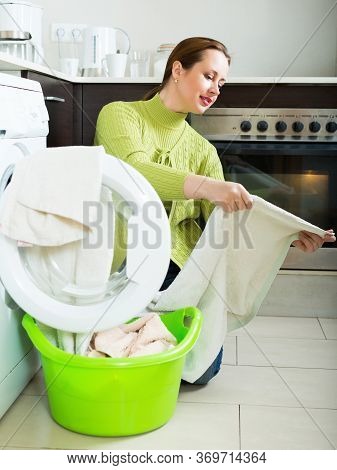 Positive Woman In Green Cheking White Clothes Near Washing Machine At Home