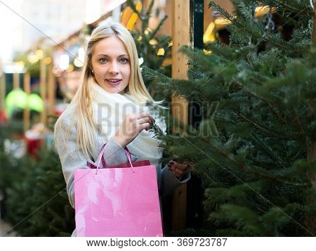 Long-haired Caucasian Beautiful Blond Woman Choosing A Fir At A Festive Marketplace
