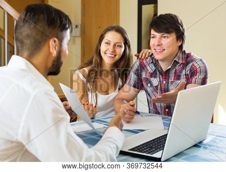 Smiling Young Couple And Salesman Talking Cheerfully About Purchase