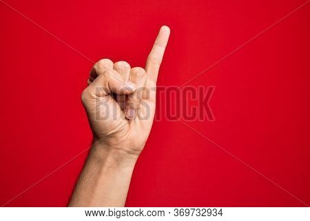 Hand of caucasian young man showing fingers over isolated red background showing little finger as pinky promise commitment, number one
