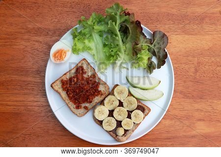 Bread With Chili Paste And Bread With Banana, Half Boiled Egg And Vegetables In The White Round Plat