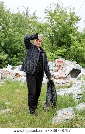 A Middle-aged Man In Black Clothes Puts Grbage In A Black Bag