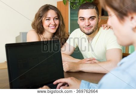 Young Married Couple Talking With Employee At The Table And Smiling.
