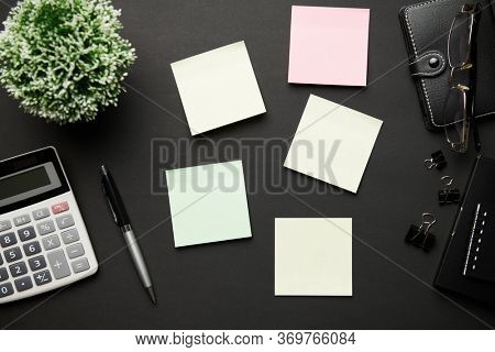 Top view of modern black office desk with calc, notebook, pen, blank sticker and a lot of things. Flat lay table layout. Copy space for text.