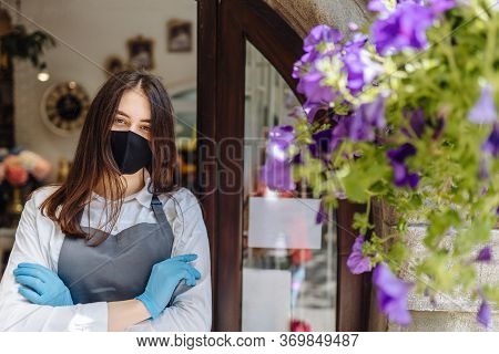 Coronavirus Covid 19. Floral Shop Woman Owner In Gloves With Face Mask, Open Door After Lockdown Qua