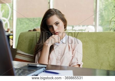 Beautiful Girl At A Table In A Cafe Is Sitting In Front Of A Laptop.