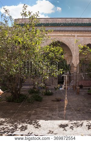 Yard With An Arcade. Wild Growing Plants. Ruins Of An Abandoned Building. Bright Blue Sky With White