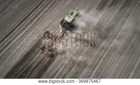 Aerial View Of A Clean Field In Which The Tractor Makes Vertical Tillage. Red Tillage Equipment And 