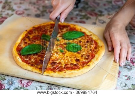Close-up Female Hand Cutting Baked Tasty Hot Homemade Italian Margarita Pizza On Wooden Cutboard And
