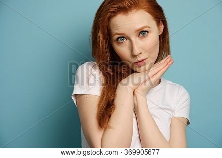 A Red-haired Girl In A White T-shirt Is Standing Against A Blue Background And Is Ingratiatingly Loo