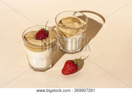 Dalgon Coffee In A Transparent Glass With Milk On A Pastel Background With Strawberries.