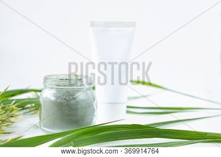Green Clay Powder In A Glass Jar, White Tube With Cream On A White Background. Spa And Body Care Con