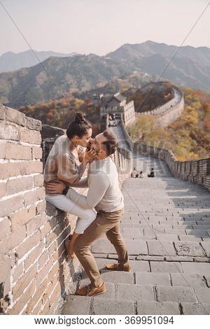 Beautiful Young Couple Sitting Down And Showing Affection At The Great Wall Of China.