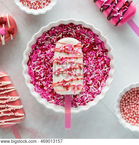 A Decorated Valentines Day Cakesicle In A Bowl Full Of Sprinkles.