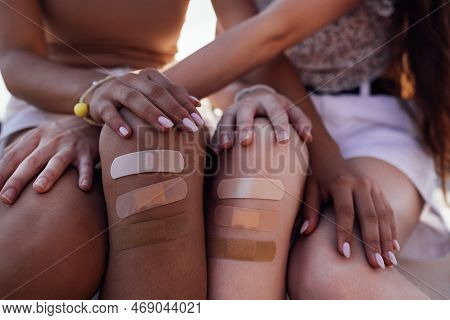 Cropped View Of Two Diffrent Races Female Teen Friends With Adhesive Plasters On Injured Knee Sittin