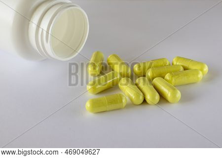 A Jar Of Food Supplements Lies Next To Sprinkled Yellow Quercetin Capsules On A White Background.