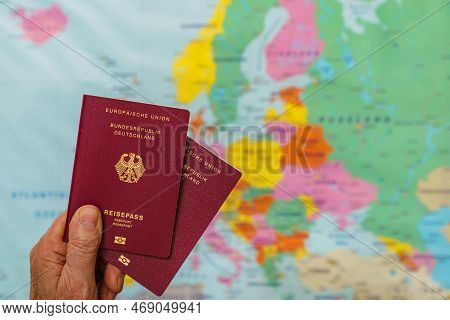 Male Hand With Two German Passports Over Map Of Europe. Close Up.
