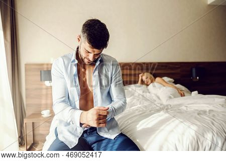 Morning After Making Love. A Man Is Sitting On The Bed And Getting Ready To Leave The Hotel Room, He