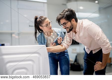 Young Couple Choosing Washing Machine While Standing In Whiteware Department.