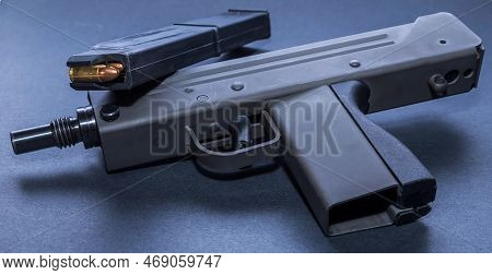 An Uzi Mini Machine Gun With A Loaded, Extended Magazine On A Black Background