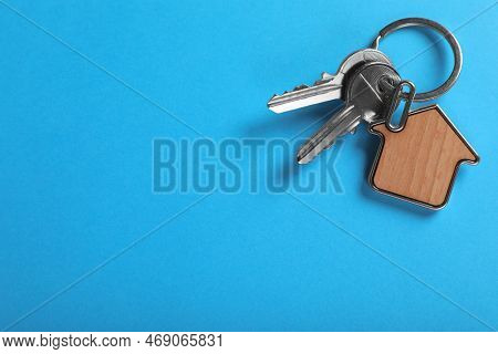 Keys With Trinket In Shape Of House On Blue Background, Top View And Space For Text. Real Estate Age