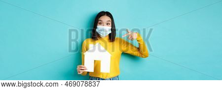 Covid-19, Pandemic And Real Estate Concept. Cheerful Asian Woman Smiling In Medical Mask, Showing Pa
