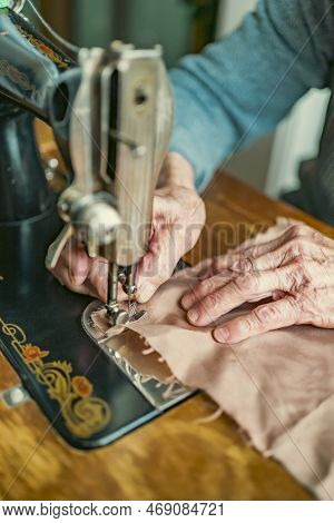 Senior woman in spectacles use sewing machine. wrinkled hands of the old seamstress.elderly woman . 