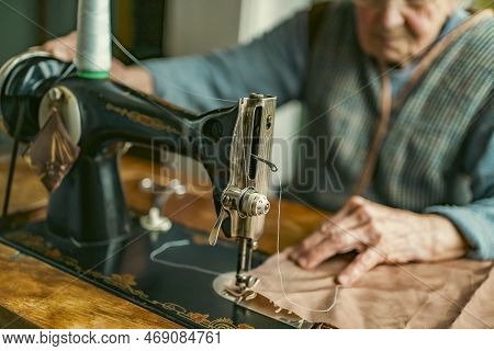 Senior woman in spectacles use sewing machine. wrinkled hands of the old seamstress.elderly woman . 