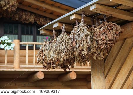 Oak Brooms Hanging Under Roof Of Wooden Sauna Outdoors