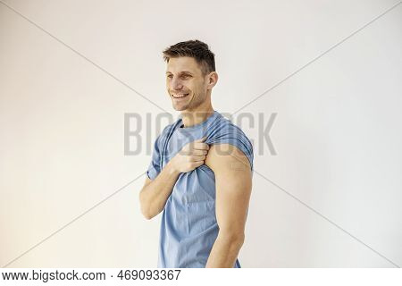 A Cheerful Man With Rolled Up Sleeve Is Showing His Vaccinated Shoulder While Standing Against The W