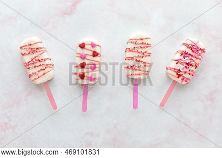 White Chocolate Coated Cakesicles For Valentines Day On A Pink Marble Surface.