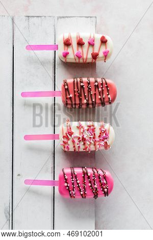 Vertical View Of Valentine Cakesicles On A White Rustic Wooden Board.