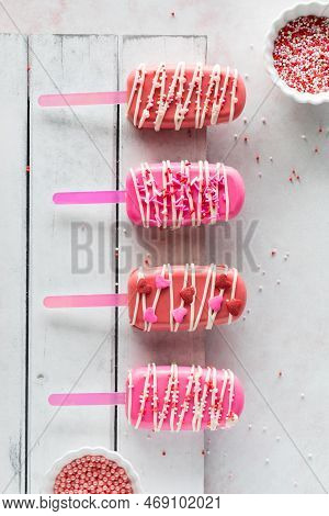 Homemade Valentine Cakesicles On A White Rustic Board With Bowls Of Sprinkles.
