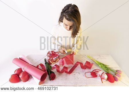 The Child Makes A Gift From Ribbons, Souvenir Hearts, Flowers And Colored Paper. Fakes For Valentine