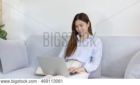 Woman using laptop to work or do homework at home with smiling face in her living room, Creating hap